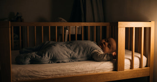 Bébé endormi sur le dos dans son lit à barreaux, éclairé par une veilleuse la nuit